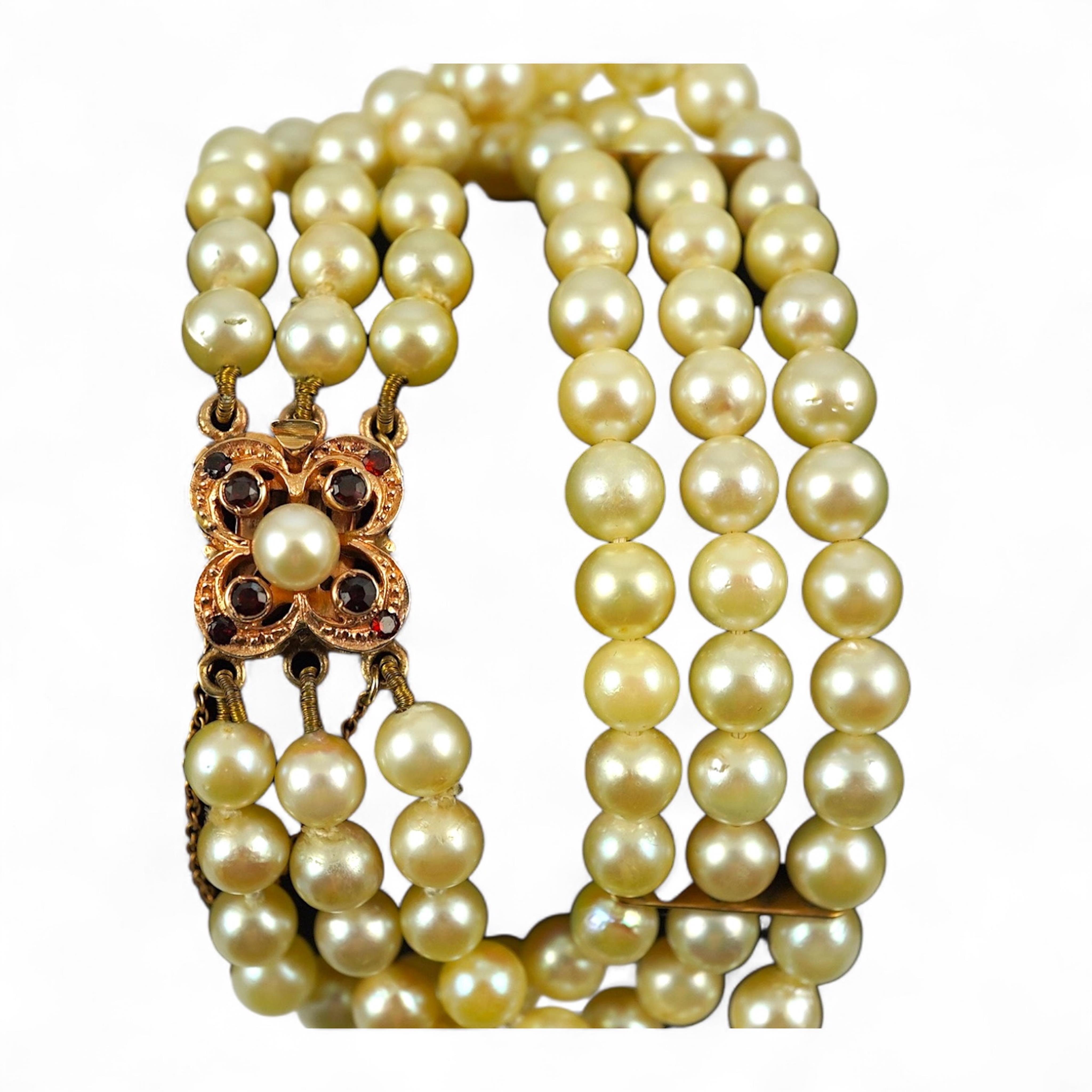 A triple strand cultured pearl bracelet, with a 9ct gold, garnet and cultured pearl cluster set clasp, 16cm.